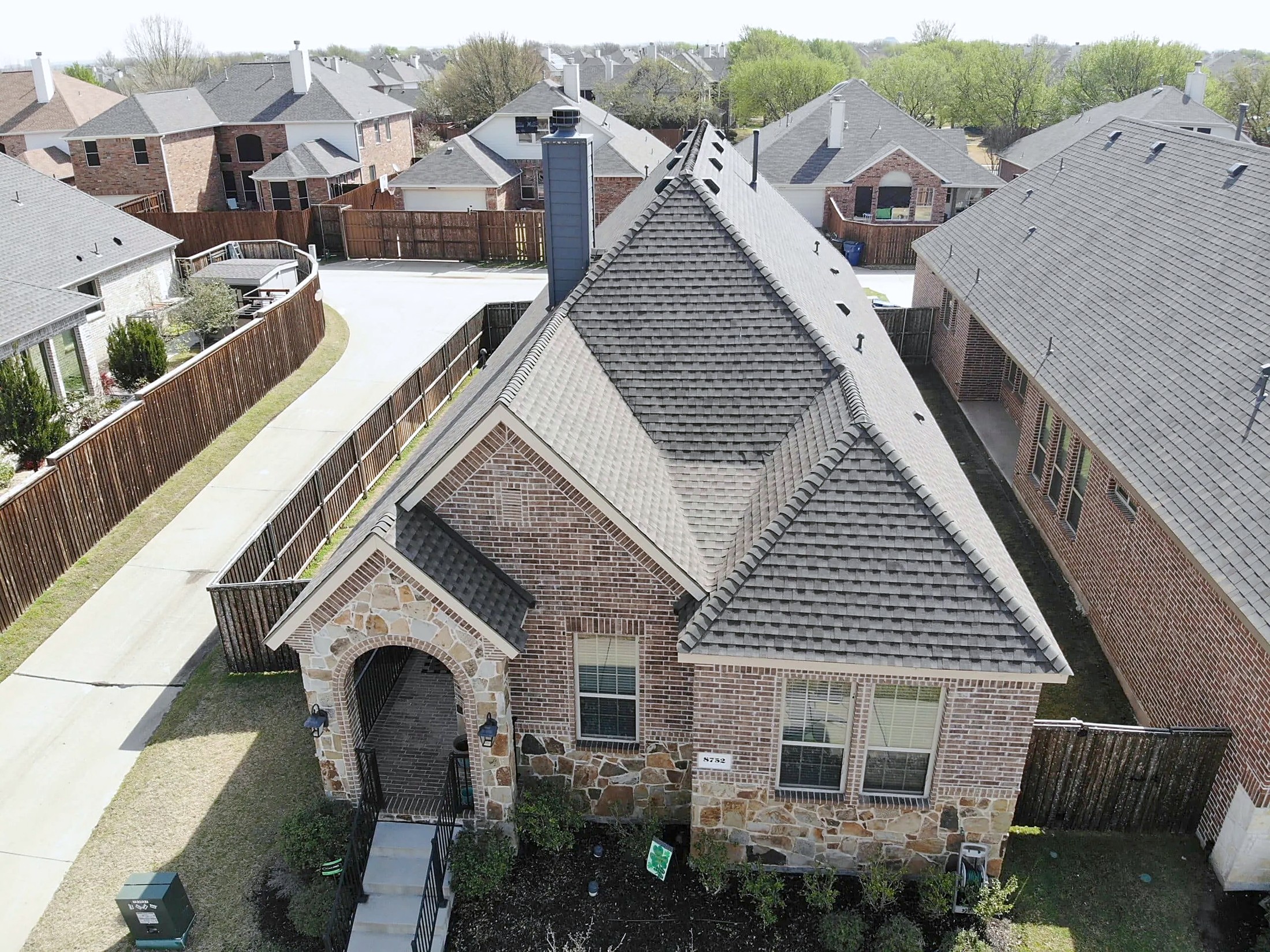Drone view of a brick and stone home with a new charcoal shingle roof