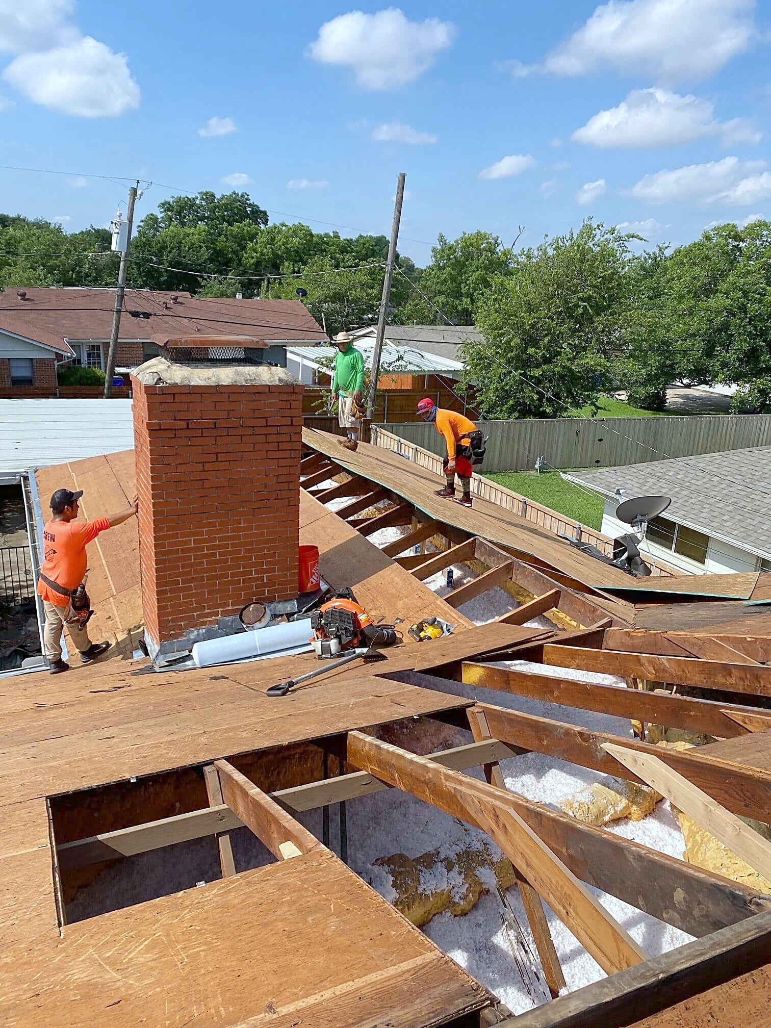 Roofers tearing off an old roof around a brick chimney, with bare decking exposed