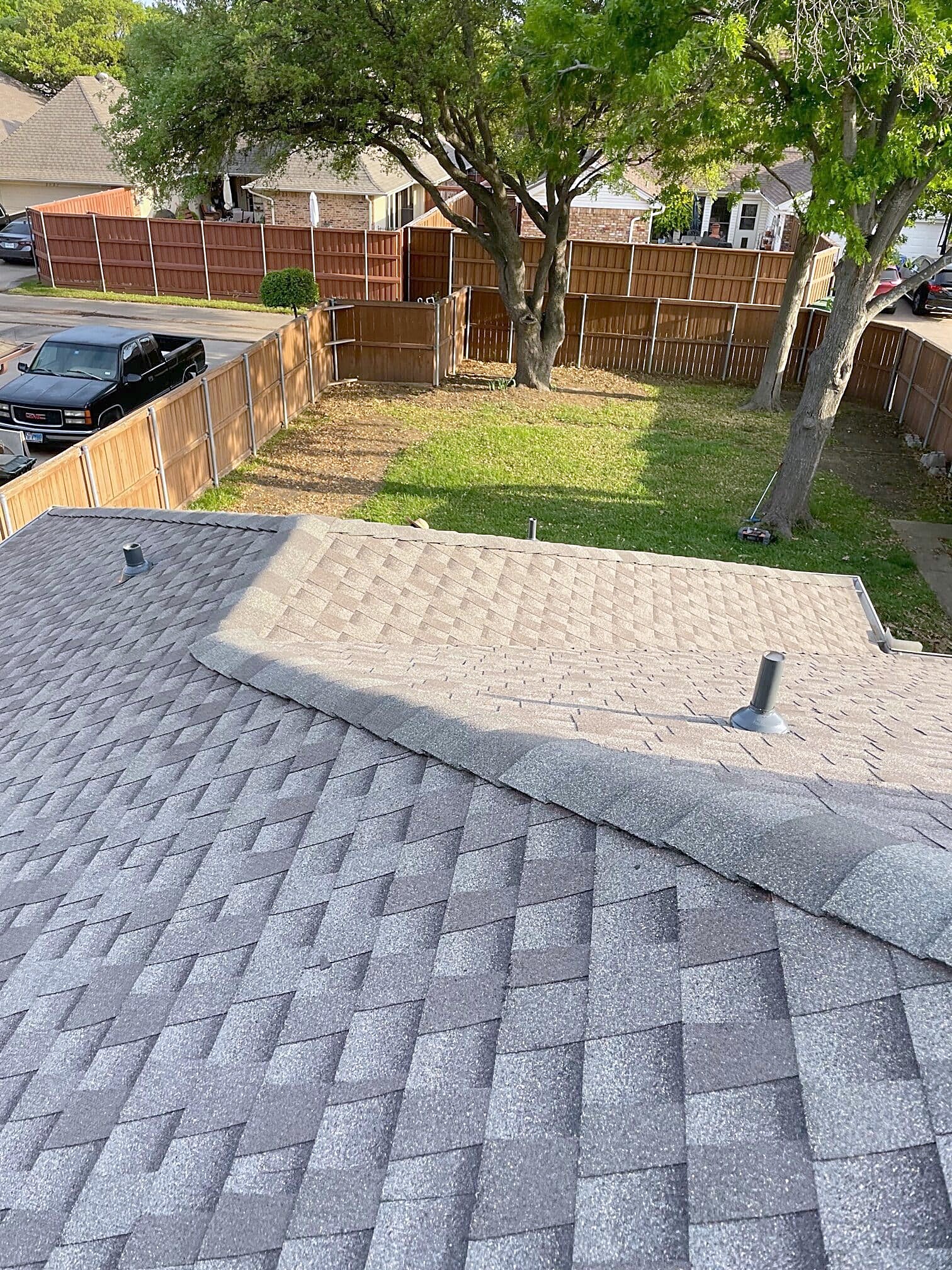 A finished shingle roof seen from the backyard of a brick home