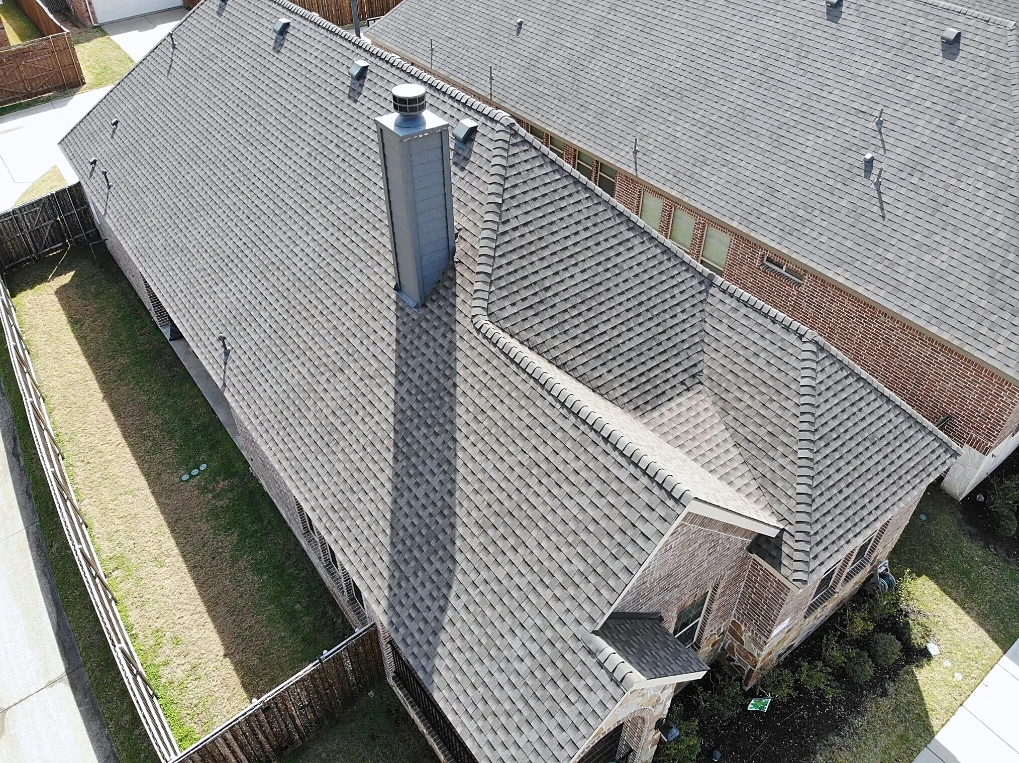 Aerial view of a finished gray shingle roof with a sided chimney chase