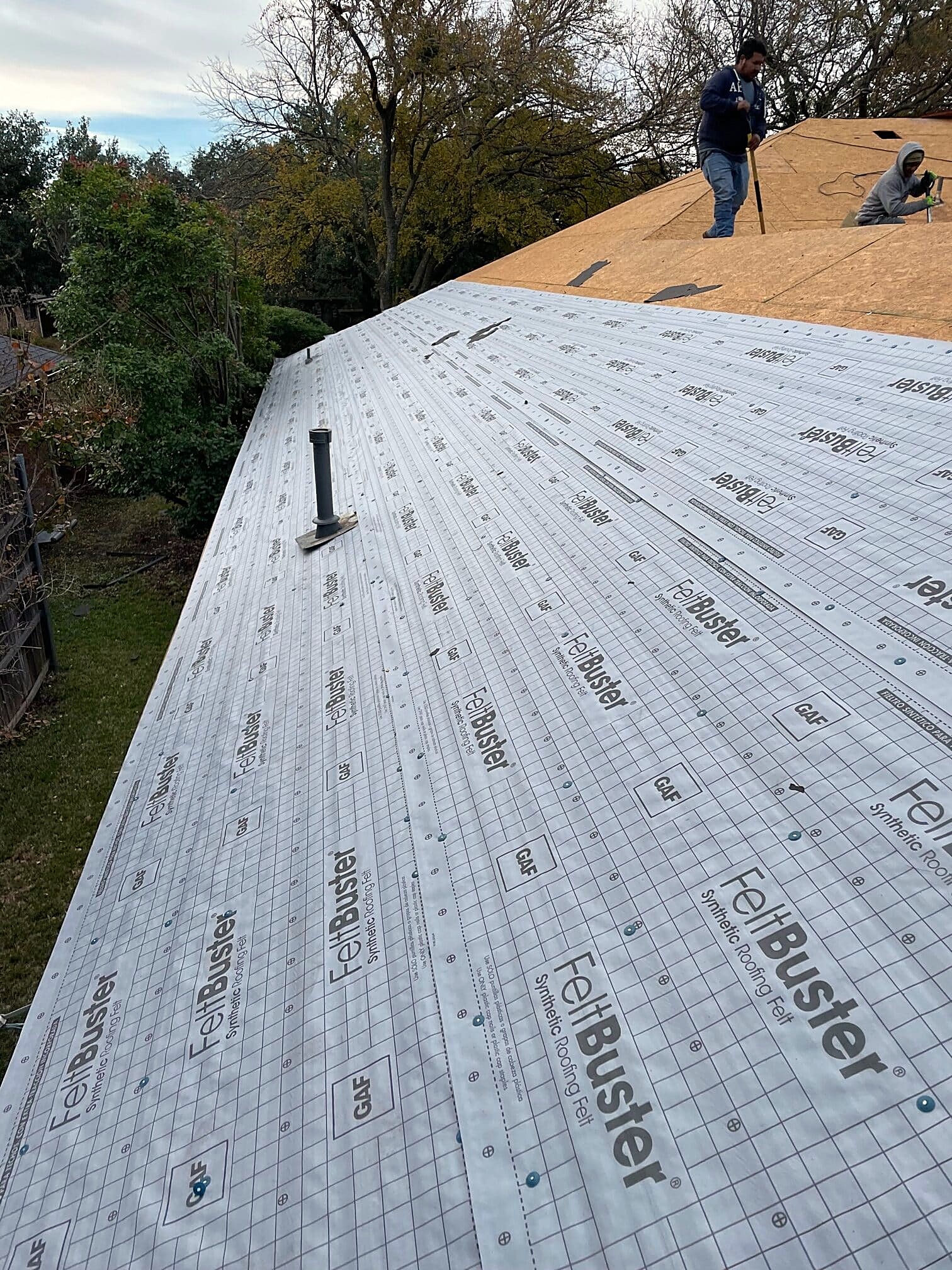 Synthetic underlayment rolled across a roof with a roofer at the ridge