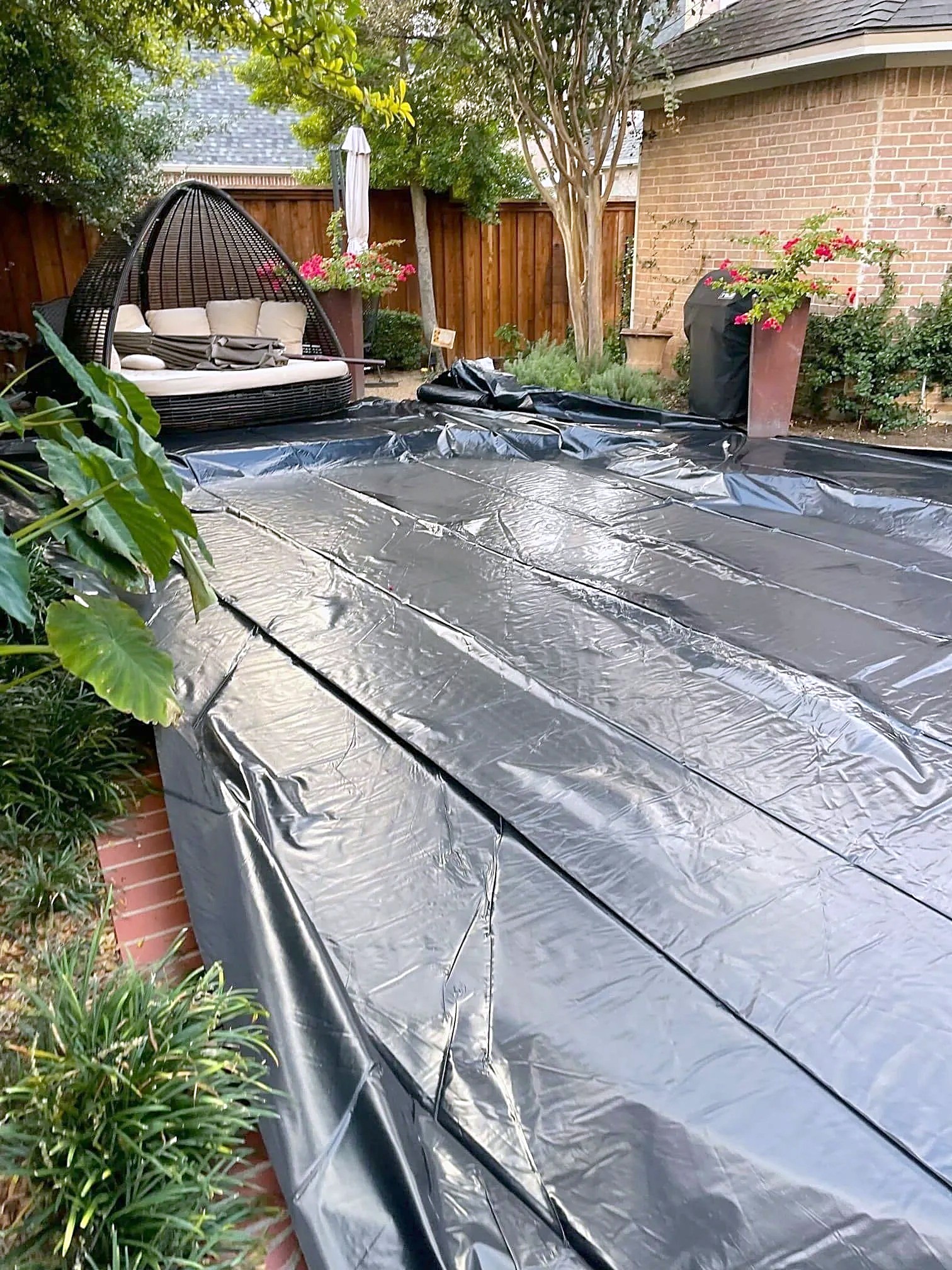 A black tarp stretched over a backyard pool beside the patio during a roof tear-off